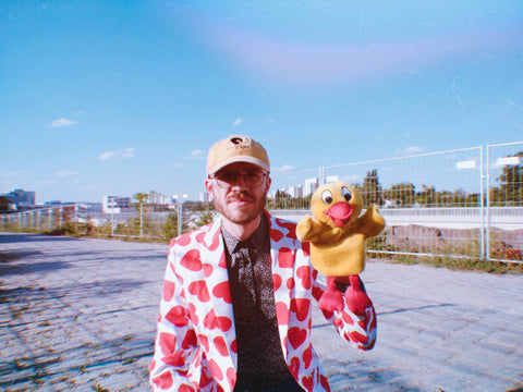 Mann mit Blazer voller Herzen und einer Entenpuppe in der Hand