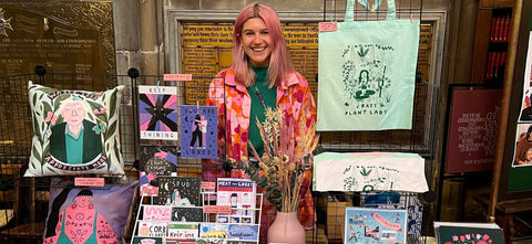 Frau steht hinter ihrem Stand voller Postkarten und Textilien