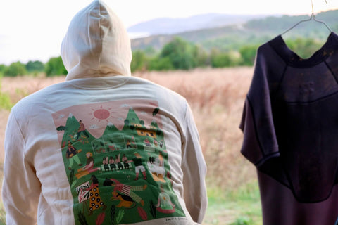 Mann sitzt vor einem Feld und trägt einen Hoodie mit buntem Rückenprint