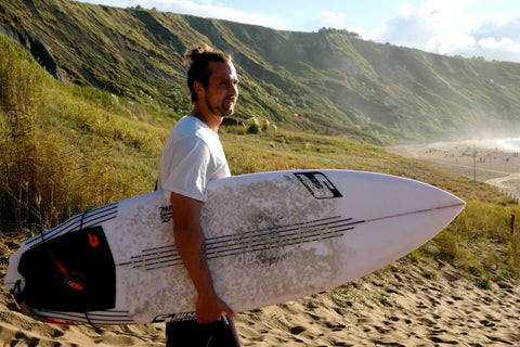 Mann am Strand mit einem Surfbrett und weißem Bio-T-Shirt